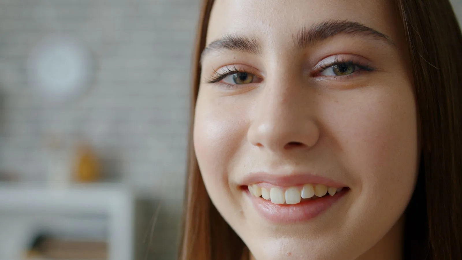 Close-up of a smiling young woman with clear skin indoors.